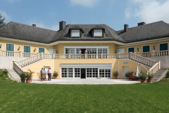 großes gelbes Gebäude mit grüner Wiese in frontaler Ansicht