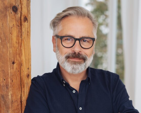 Mann an Holzsäule gelehnt mit Blick in die Kamera