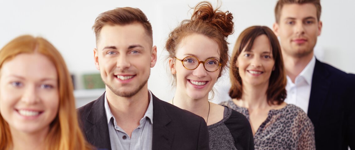 Fünf Mitarbeitende hintereinander aufgestellt von schräg rechts fotografiert mit Blick in die Kamera